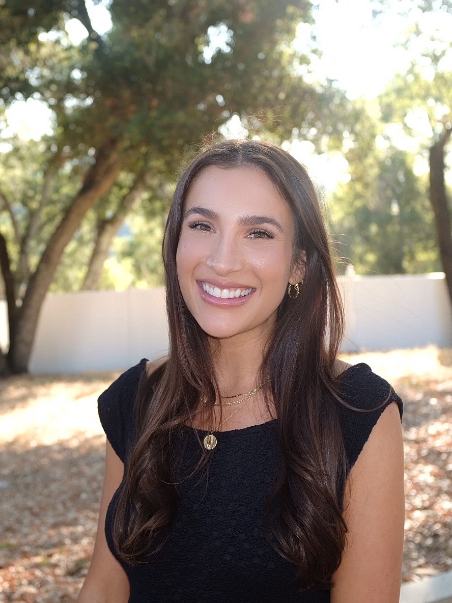 Smiling woman in a sunny outdoor setting.